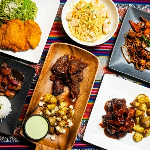 Assortment of Peruvian dishes, including lomo saltado, fried chicken, pasta, and short ribs, on a colorful tablecloth.