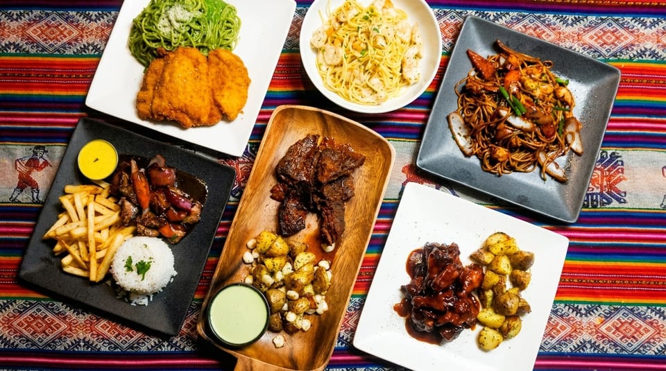 Assortment of Peruvian dishes, including lomo saltado, fried chicken, pasta, and short ribs, on a colorful tablecloth.