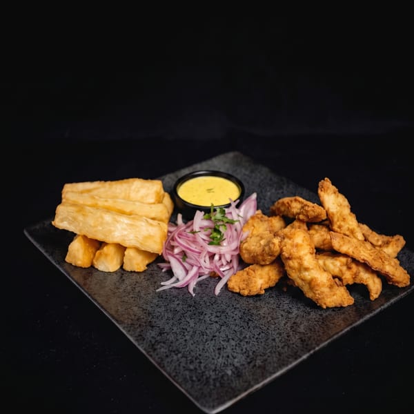 Fried fish strips, yucca fries, red onion salad, and yellow dipping sauce on a dark plate.