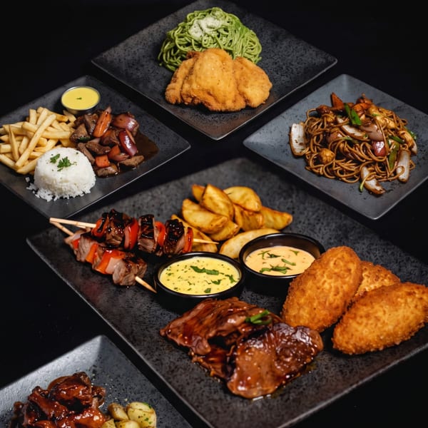 An overhead shot of various Peruvian dishes, including lomo saltado, green spaghetti, and anticuchos, on black plates.