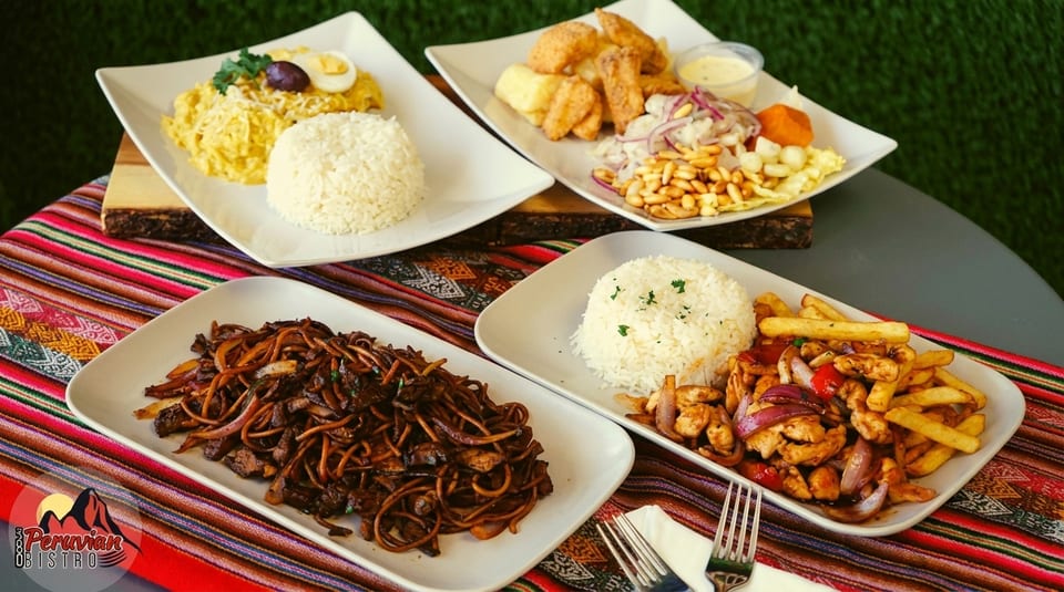 Four plates of Peruvian dishes, including lomo saltado, aji de gallina, and fried seafood, on a colorful striped tablecloth.