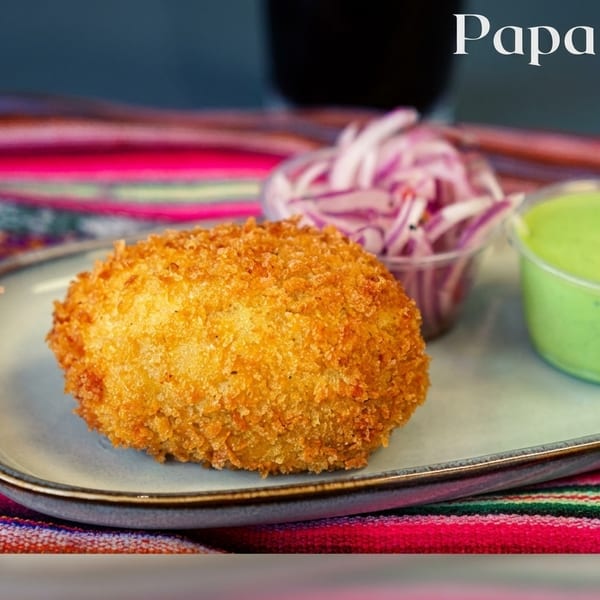 Golden-fried Papa Rellena with red onions and green sauce on a plate over a colorful striped cloth.