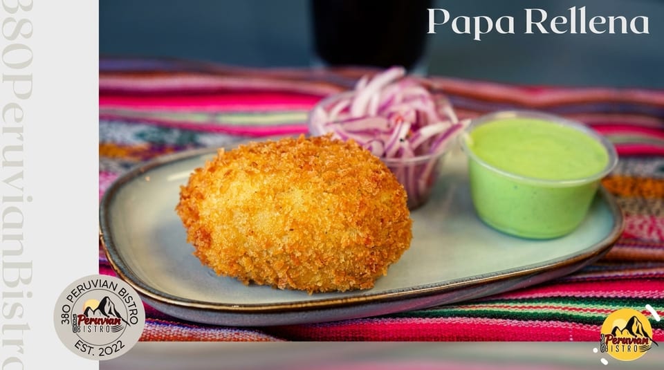 Golden-fried Papa Rellena with red onions and green sauce on a plate over a colorful striped cloth.