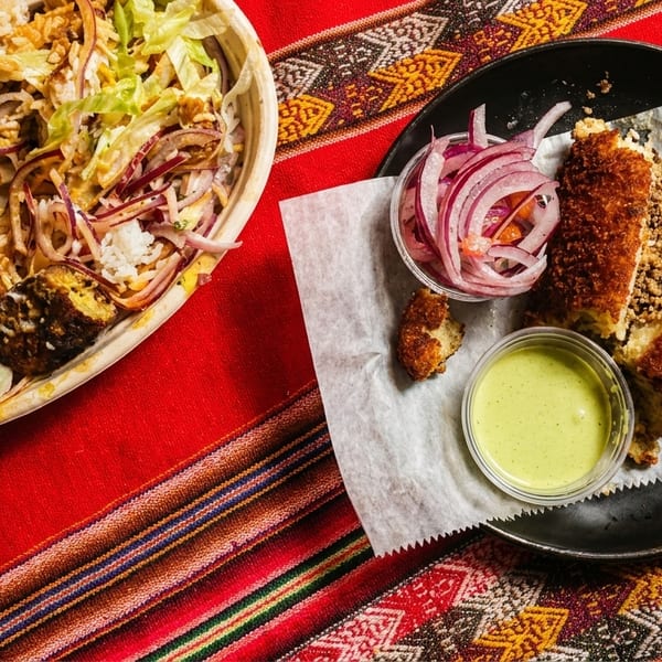 Peruvian food on a colorful striped tablecloth, featuring a rice bowl and a fried stuffed potato.