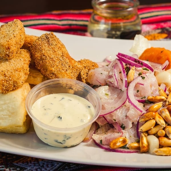 Peruvian ceviche with fried fish, yuca, corn, and a creamy sauce on a white plate.