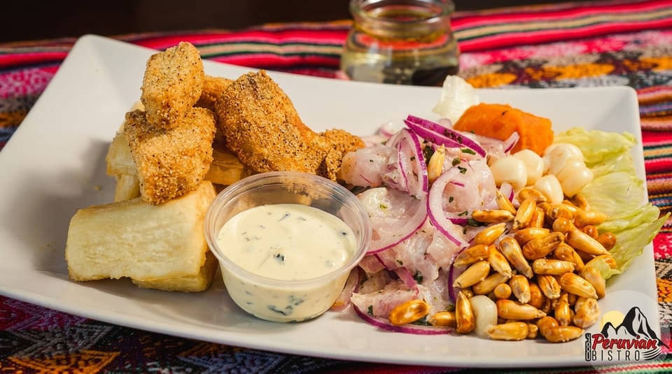 Peruvian ceviche with fried fish, yuca, corn, and a creamy sauce on a white plate.