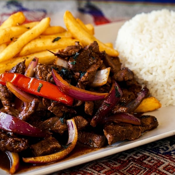 Peruvian Lomo Saltado with beef, red onions, peppers, fries, and white rice on a plate.
