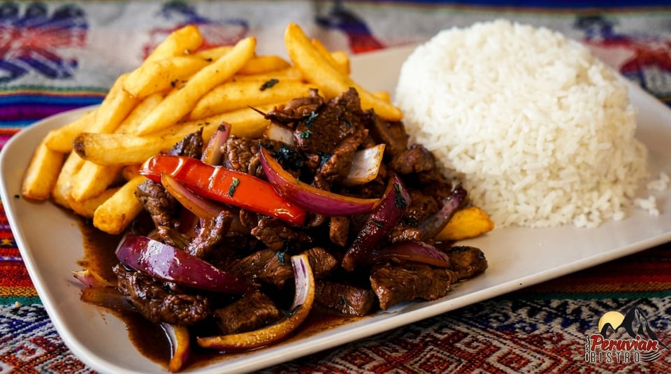 Peruvian Lomo Saltado with beef, red onions, peppers, fries, and white rice on a plate.